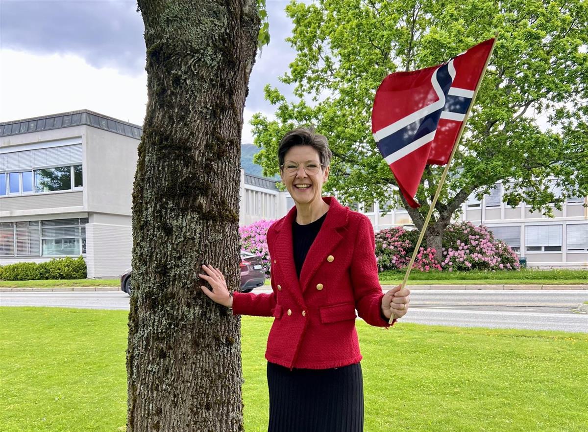 Ordførar Judith Kvåle i Maurstadparken med rådhuset i bakgrunnen. Held eit norsk flagg. - Klikk for stort bilete